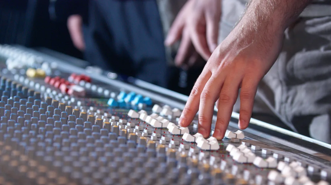 Hands adjusting the controls of a sound mixing console
