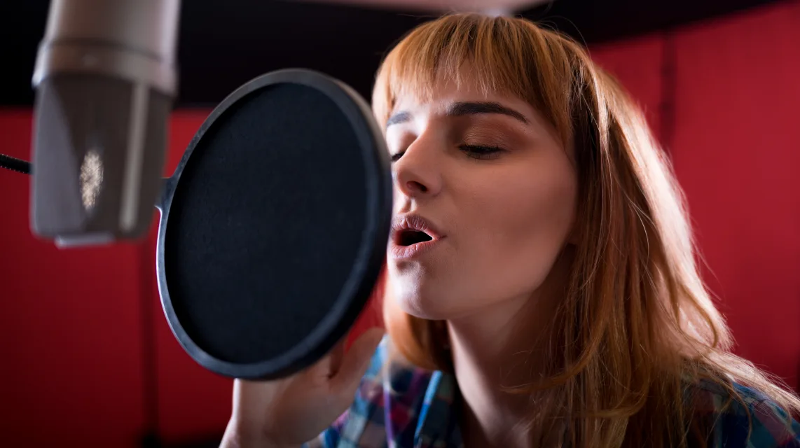 Vocalist recording into a condenser microphone in a booth